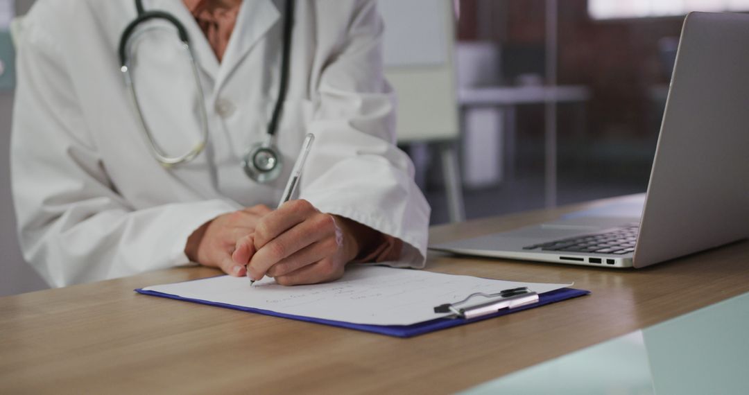 Doctor Writing Notes at Desk with Laptop - Free Images, Stock Photos and Pictures on Pikwizard.com