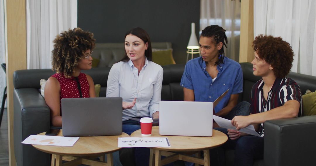 Woman leading diverse team in informal lounge meeting with laptops, charts, collaboration