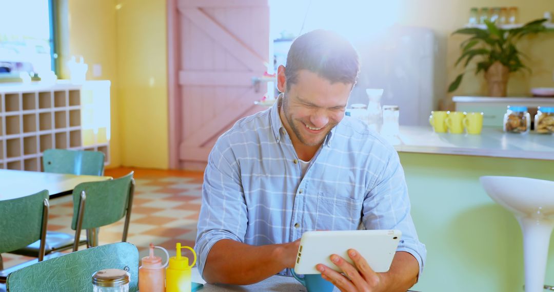 Man Smiling While Checking Tablet in Bright Café - Free Images, Stock Photos and Pictures on Pikwizard.com