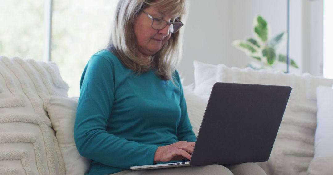 Senior woman with glasses using laptop on comfortable couch - Free Images, Stock Photos and Pictures on Pikwizard.com