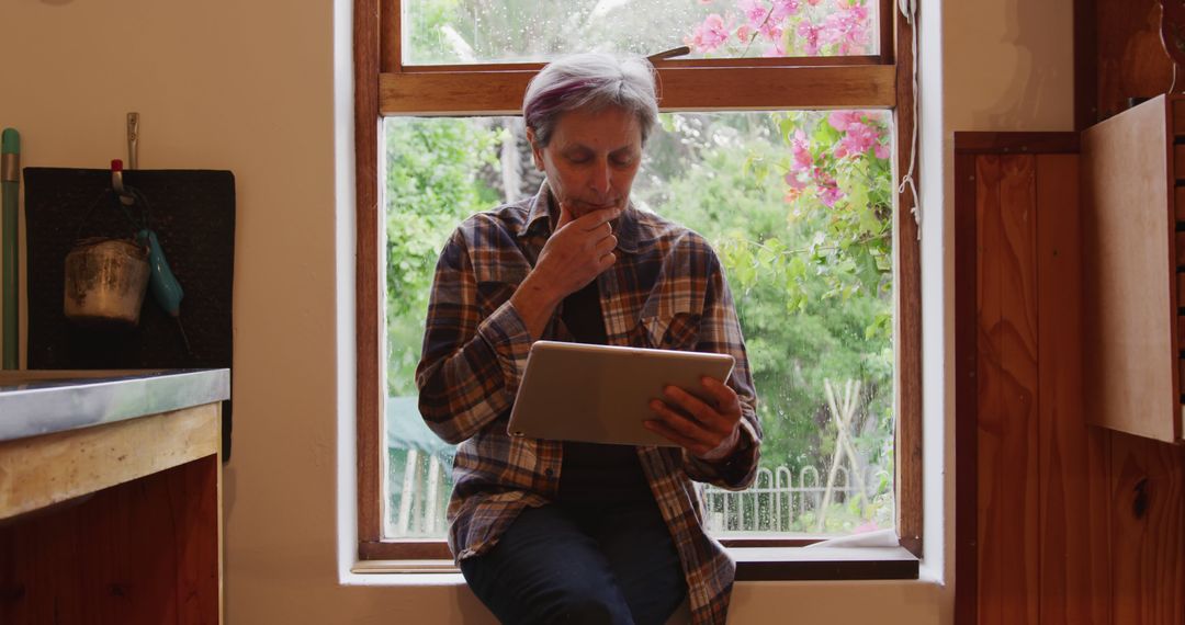 Senior Woman Reading Tablet in Cozy Kitchen Near Window - Free Images, Stock Photos and Pictures on Pikwizard.com