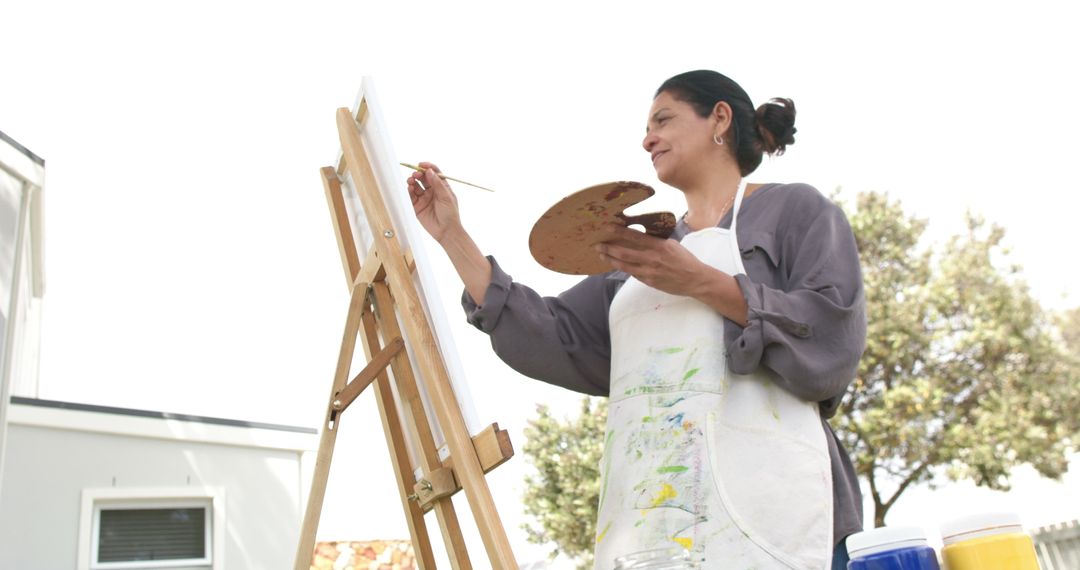 Female Artist Smiling and Painting at Easel Outdoors - Free Images, Stock Photos and Pictures on Pikwizard.com