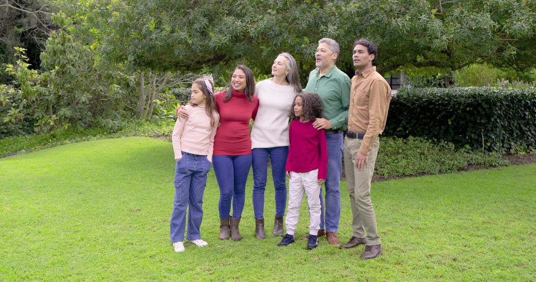 Multigenerational diverse family posing outdoors under tree in casual sweaters and jeans