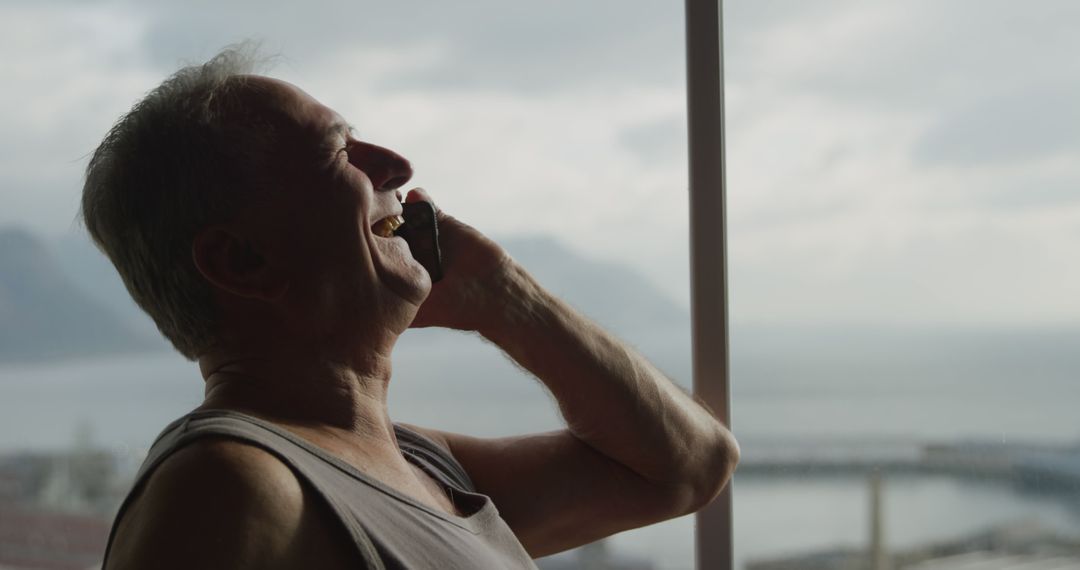 Happy Senior Man Talking on Phone by Window with Scenic View - Free Images, Stock Photos and Pictures on Pikwizard.com