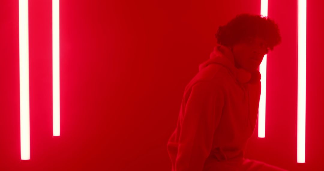 Man With Headphones Leaning on Neon Red Light Wall