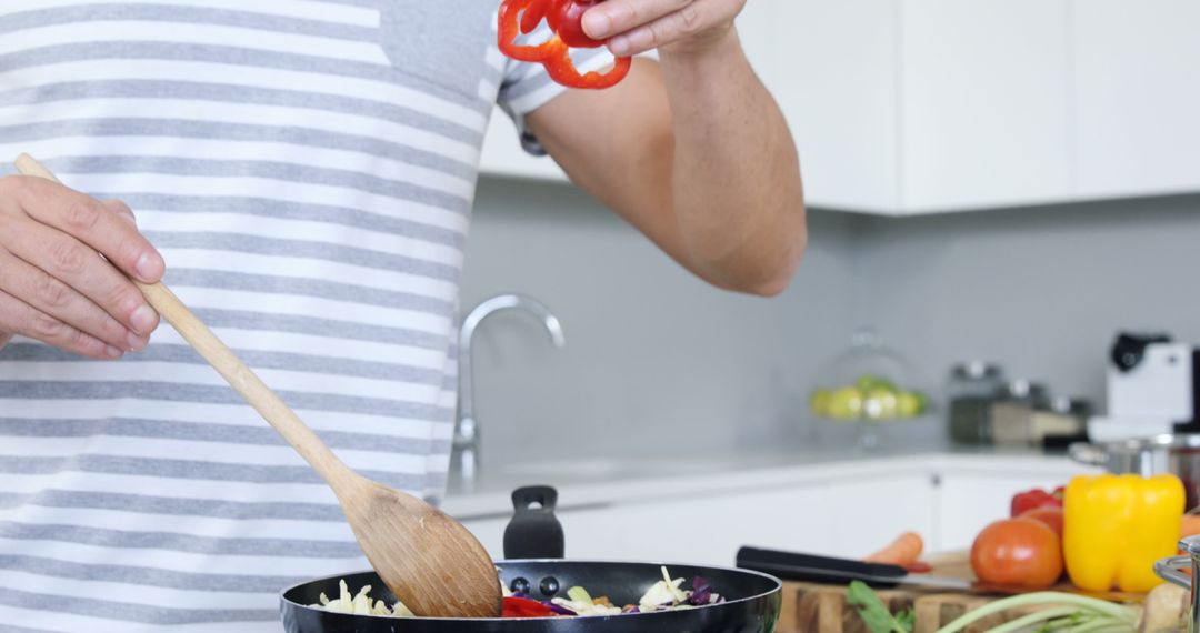 Man cooking in modern kitchen adding red bell pepper to frying pan - Free Images, Stock Photos and Pictures on Pikwizard.com