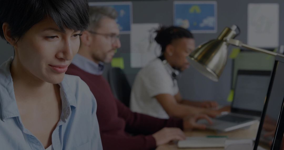 Focused woman typing at laptop in modern open-plan office with collaborative team