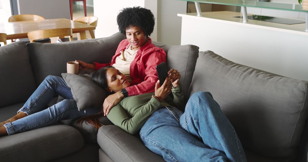 Diverse Couple Relaxing Together on Cozy Sofa Viewing something on Smartphone