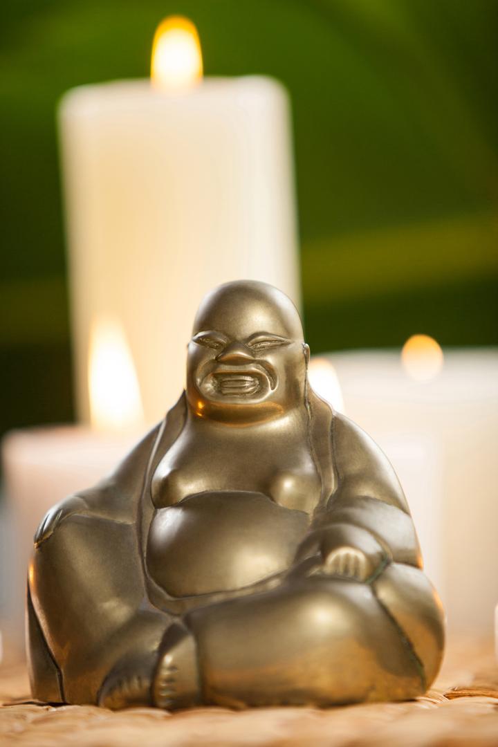 Laughing buddha figurine and lit candles on mat - Free Images, Stock Photos and Pictures on Pikwizard.com