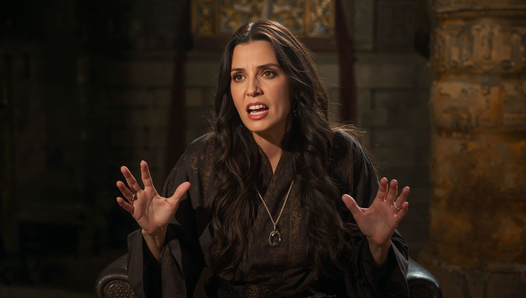 Medieval storyteller in dark robe gesturing with ringed hands and pendant, ancient stone interior