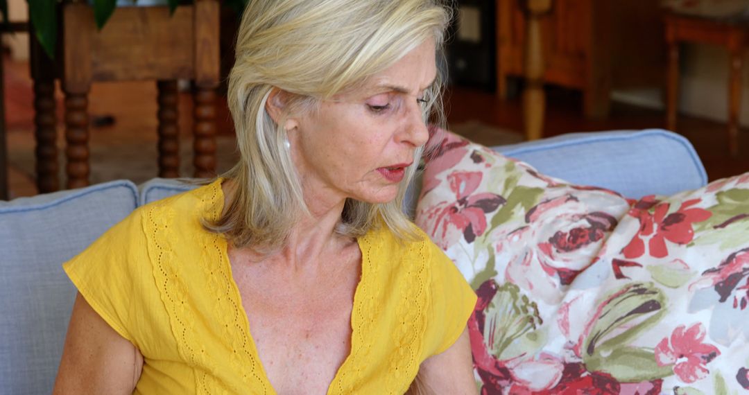 Mature Woman Sitting on Couch with Floral Pillow in Cozy Living Room - Free Images, Stock Photos and Pictures on Pikwizard.com