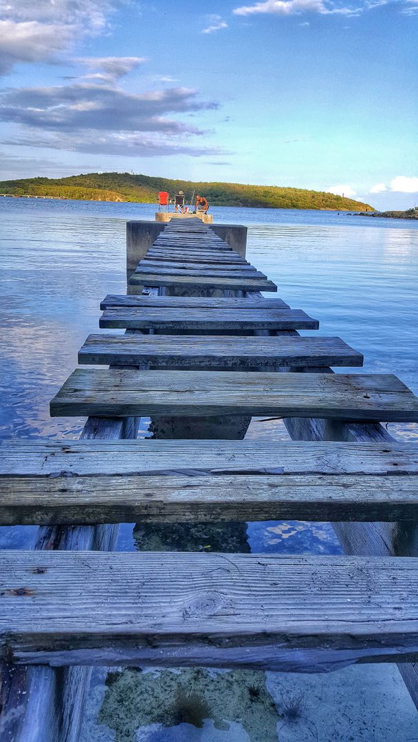 Rustic Wooden Pier Extending into Serene Blue Waters with Hills in Background - Free Images, Stock Photos and Pictures on Pikwizard.com