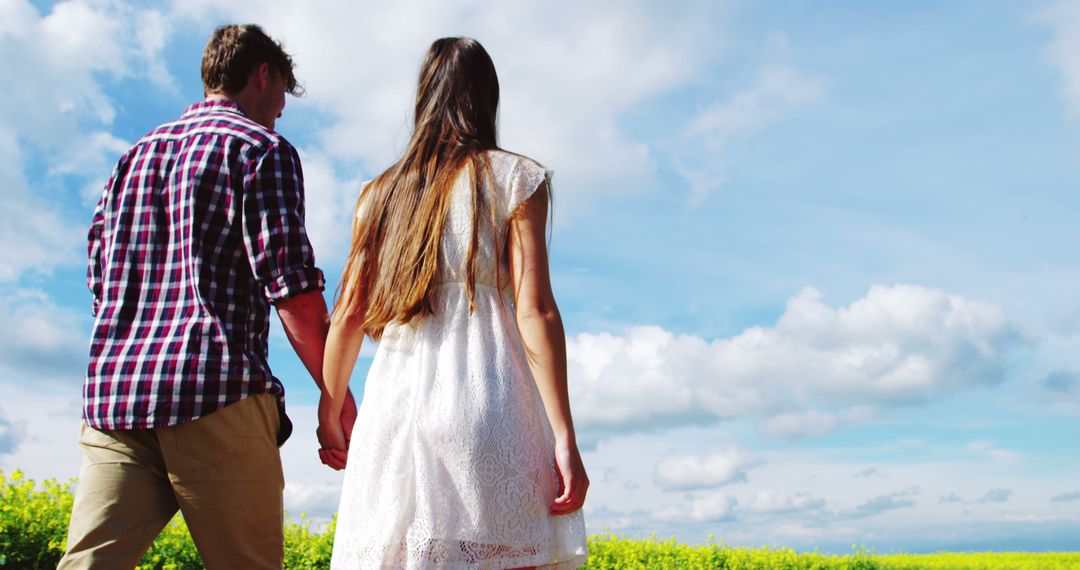 Young couple holding hands in field under sunny sky - Free Images, Stock Photos and Pictures on Pikwizard.com