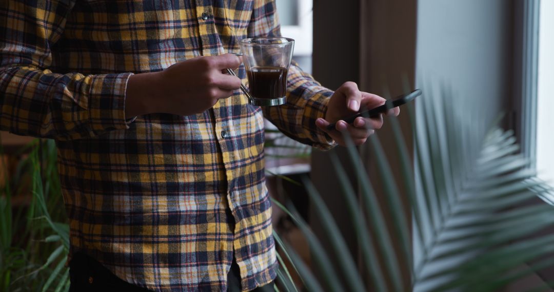 Person Holding Coffee and Smartphone Indoors Near Window with Plant - Free Images, Stock Photos and Pictures on Pikwizard.com