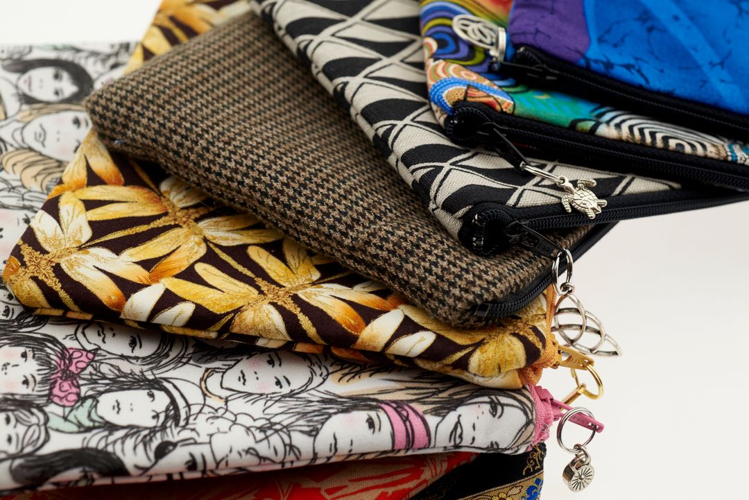 Stacked patterned fabric pouches with zipper charms showcasing floral, geometric and tweed