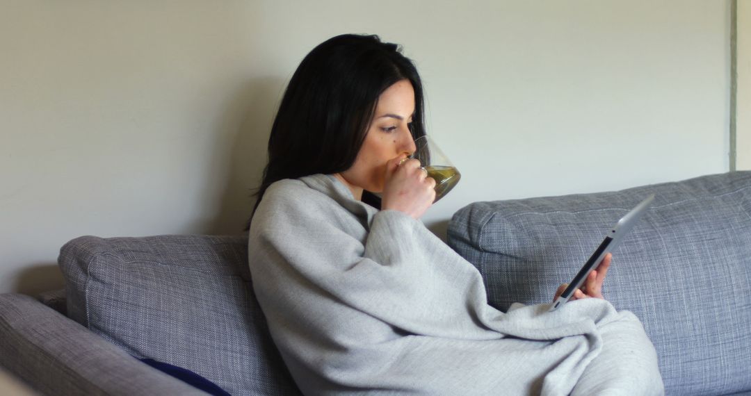 Woman Relaxing on Couch Drinking Tea and Reading Tablet - Free Images, Stock Photos and Pictures on Pikwizard.com