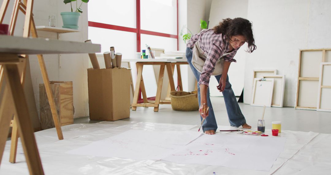 Image of biracial female artist painting on floor in studio - Free Images, Stock Photos and Pictures on Pikwizard.com