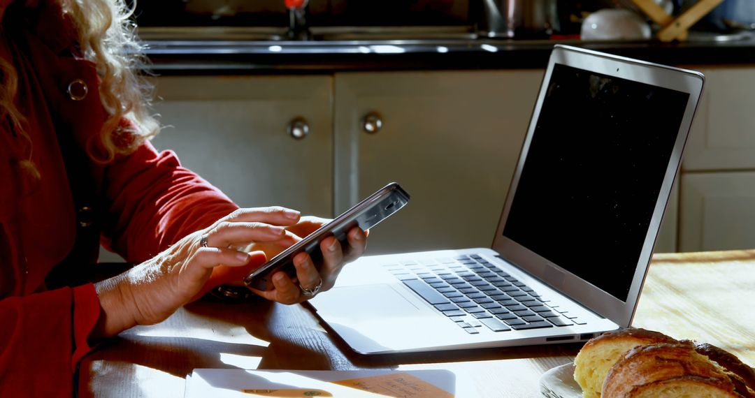 Woman Typing on Phone and Using Laptop in Home Kitchen - Free Images, Stock Photos and Pictures on Pikwizard.com