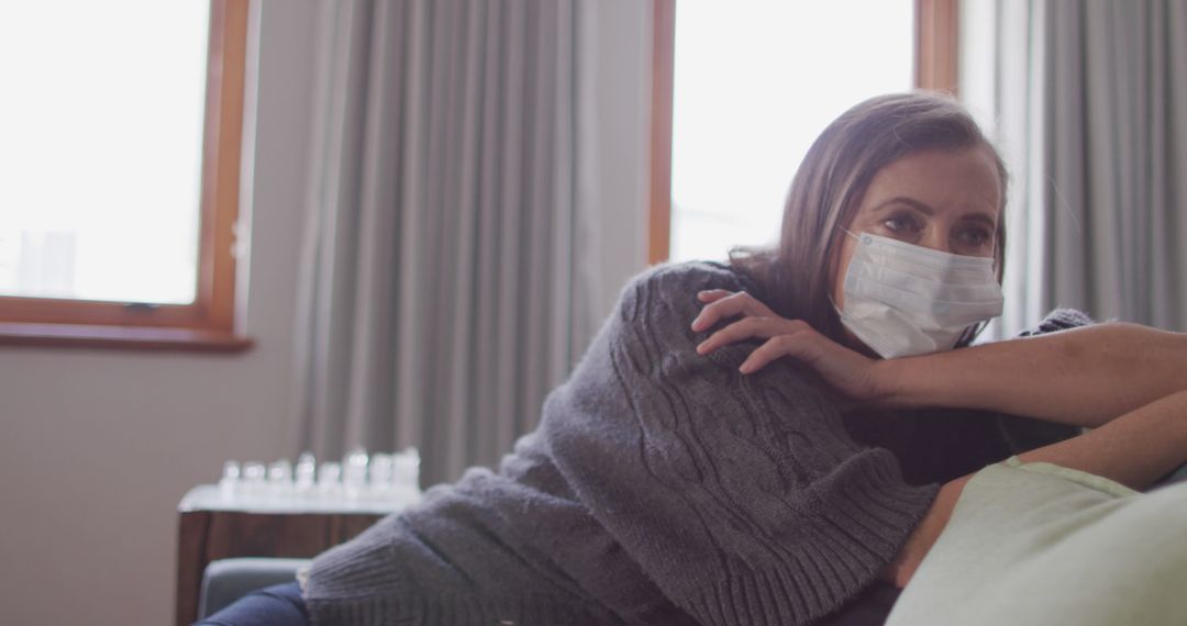 Woman wearing face mask leaning on couch at home during daytime - Free Images, Stock Photos and Pictures on Pikwizard.com