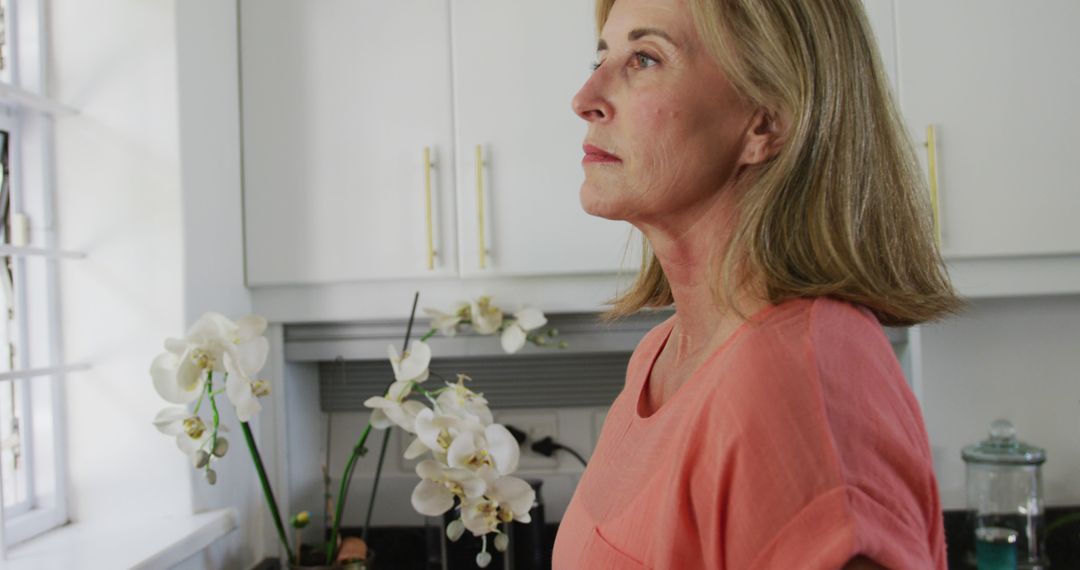 Thoughtful Woman in Kitchen with Orchids - Free Images, Stock Photos and Pictures on Pikwizard.com