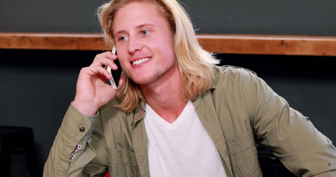Smiling Young Man with Long Blond Hair Talking on Smartphone - Free Images, Stock Photos and Pictures on Pikwizard.com