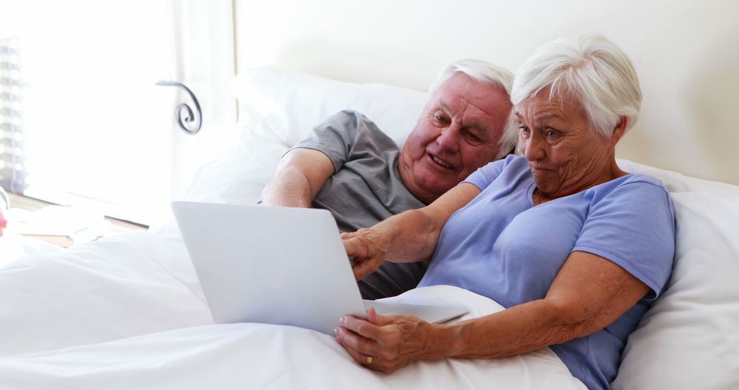 Senior couple lying in bed using laptop together engaged and smiling - Free Images, Stock Photos and Pictures on Pikwizard.com