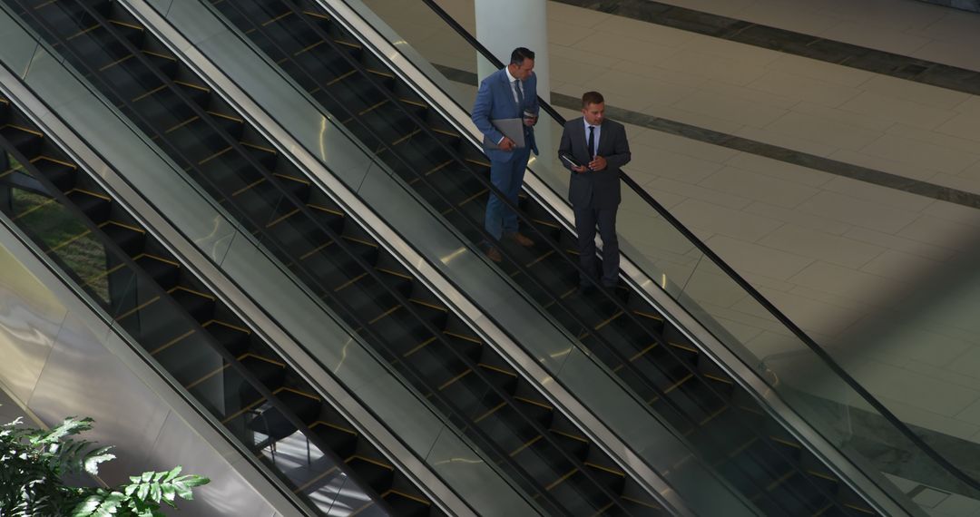 Businessmen Discussing Work on Escalator in Modern Office - Free Images, Stock Photos and Pictures on Pikwizard.com