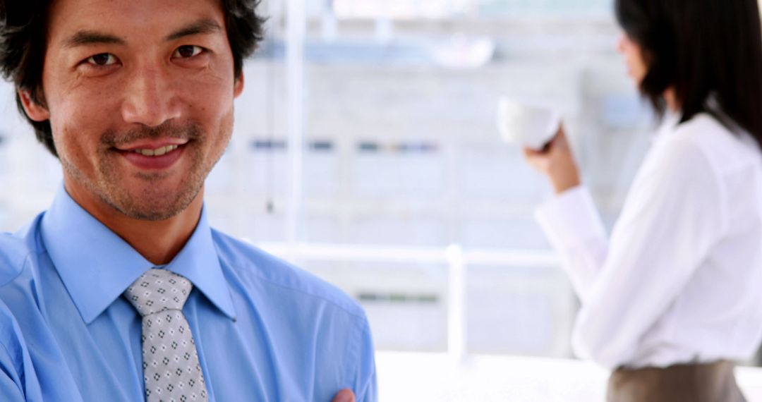 Confident businessman smiling in office with colleague in background - Free Images, Stock Photos and Pictures on Pikwizard.com