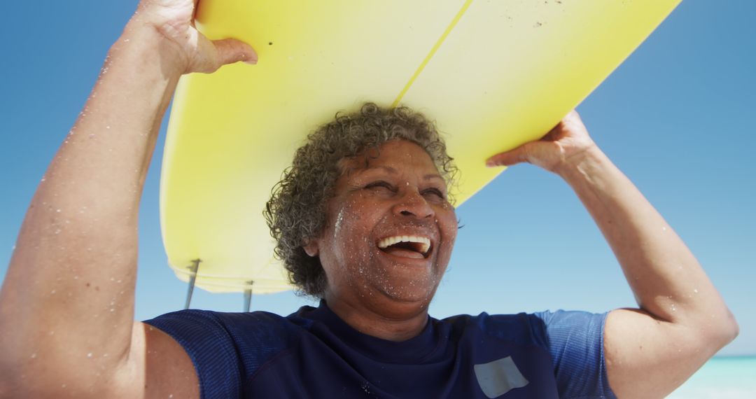 Senior Woman Joyfully Carrying Surfboard on Sunny Beach - Free Images, Stock Photos and Pictures on Pikwizard.com