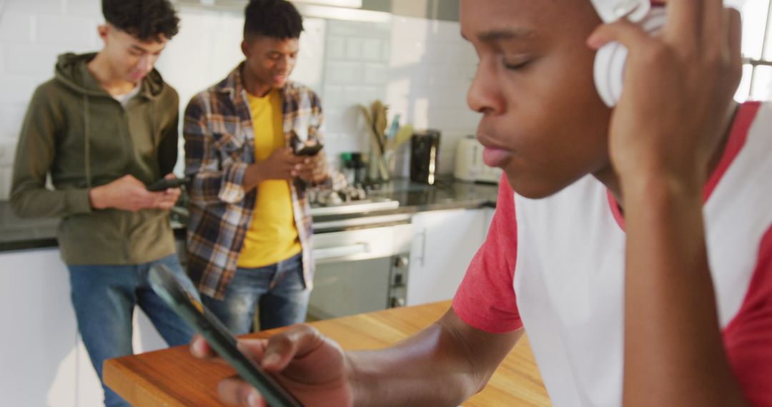 Teenagers Using Smartphones and Headphones in Modern Kitchen - Free Images, Stock Photos and Pictures on Pikwizard.com