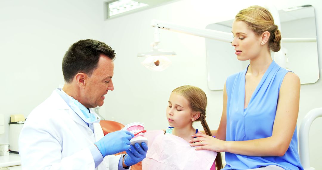 Dentist explaining tooth model to young girl with mother in clinic - Free Images, Stock Photos and Pictures on Pikwizard.com