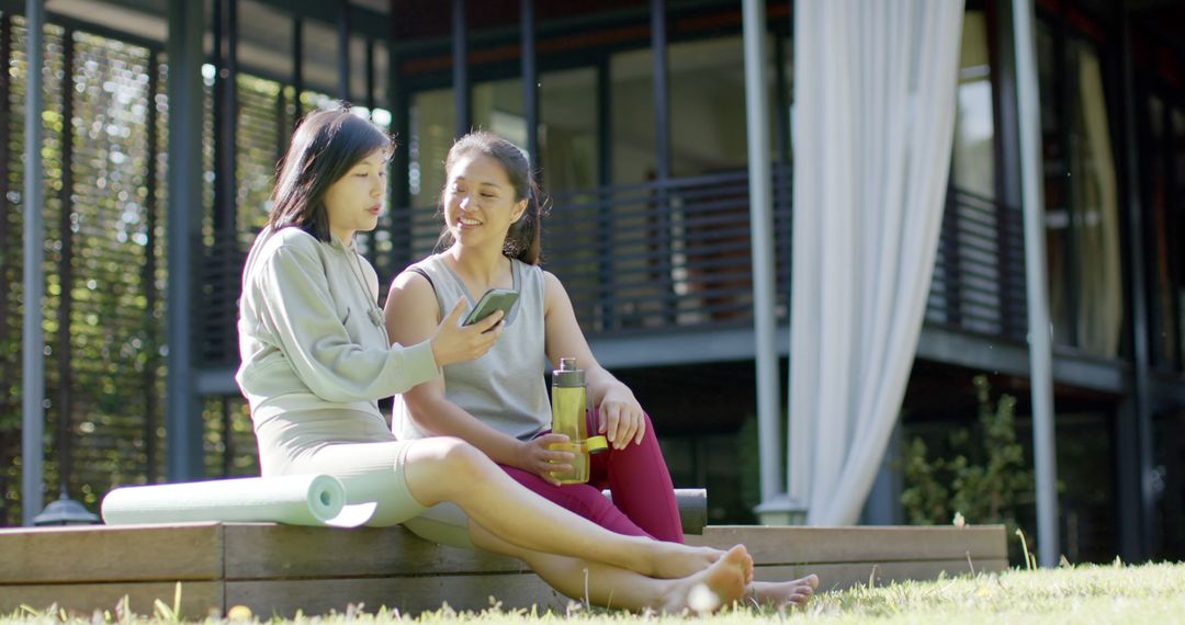 Two women enjoying outdoor relaxation while discussing fitness on smartphone - Free Images, Stock Photos and Pictures on Pikwizard.com