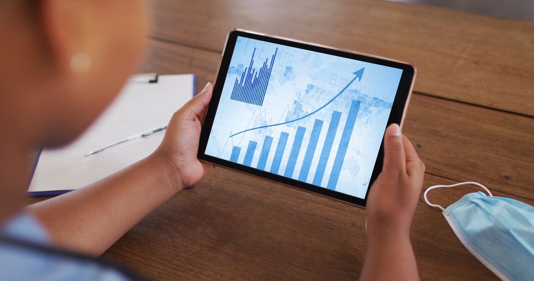 Person Analyzing Data on Tablet with Mask Nearby Indicating COVID-19 Context