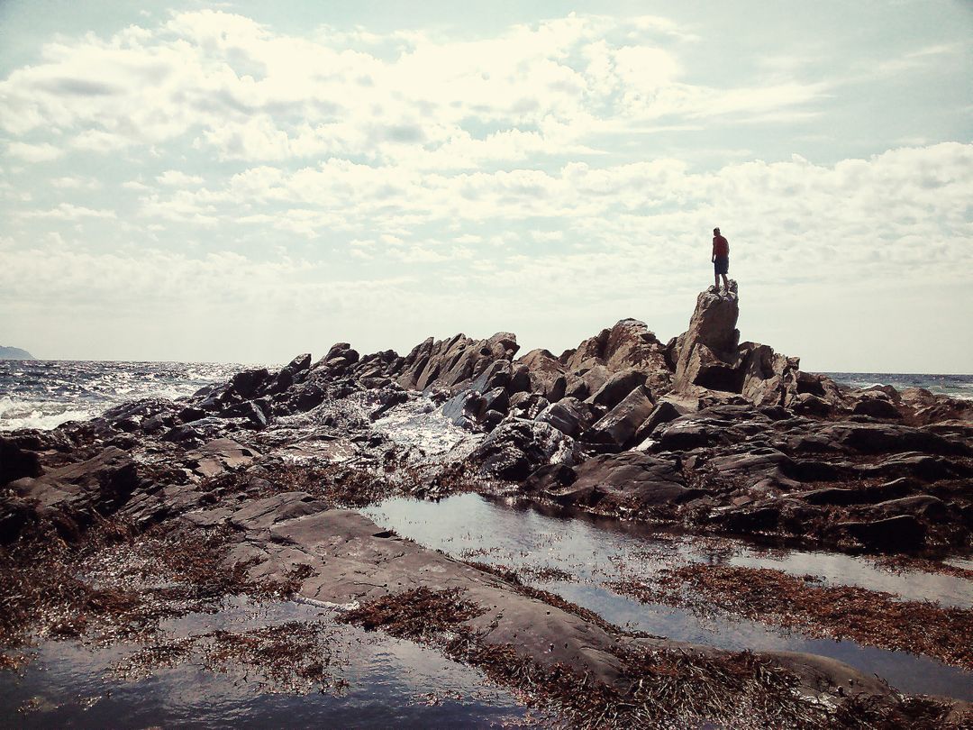 Person Standing on Rugged Rock Formation by Ocean Under Cloudy Sky - Free Images, Stock Photos and Pictures on Pikwizard.com