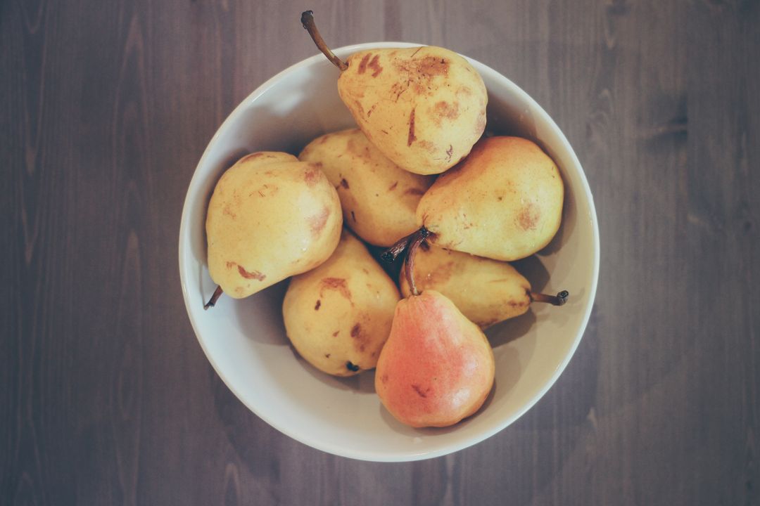 Overhead bowl holding ripe yellow and red pears on rustic wooden table, natural fruit still life