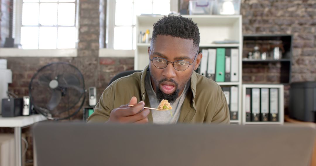 Focused Black Man Eating Lunch While Working on Laptop in Office Setting - Free Images, Stock Photos and Pictures on Pikwizard.com