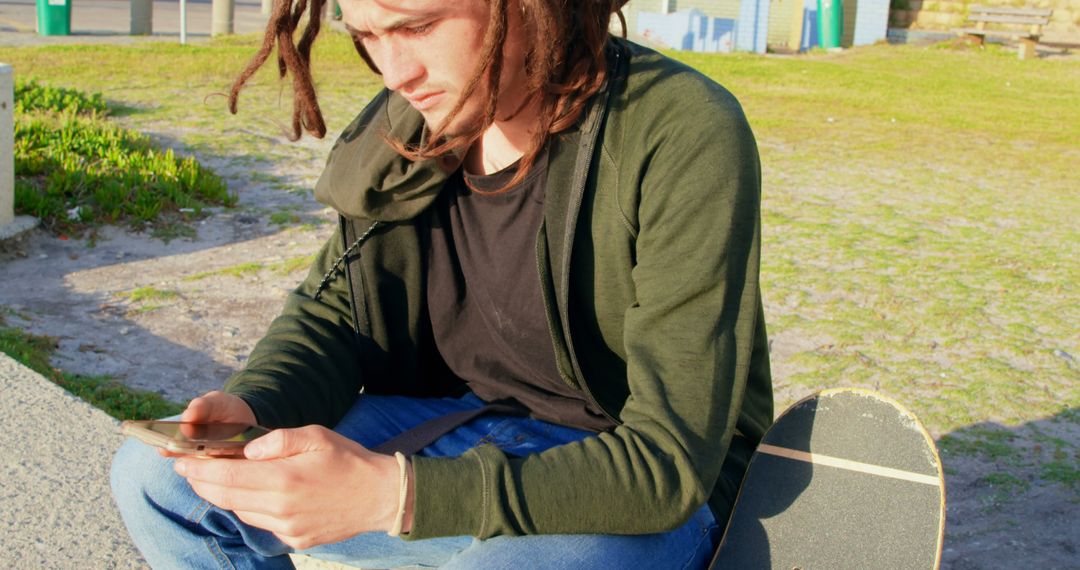 Young Man with Dreadlocks Using Smartphone Relaxing in Park - Free Images, Stock Photos and Pictures on Pikwizard.com