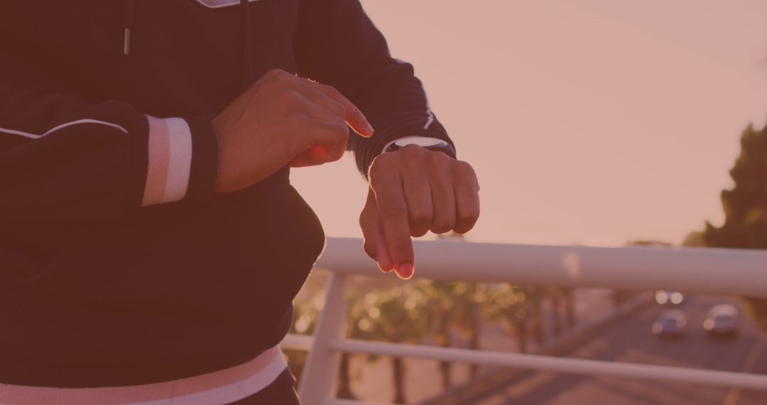 Person Utilizing Smartwatch on Urban Bridge at Sunset