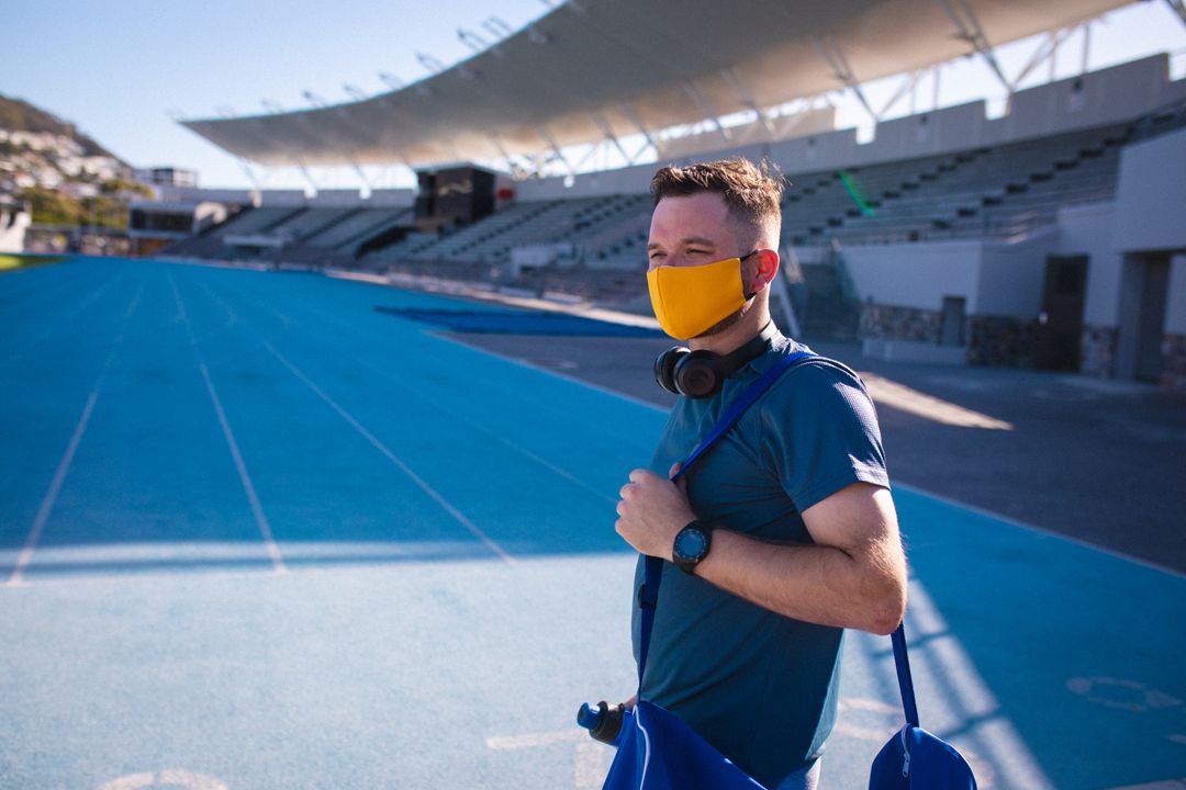 Male Athlete Wearing Face Mask Standing on Stadium Track - Free Images, Stock Photos and Pictures on Pikwizard.com
