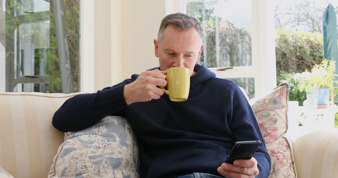 Middle-aged man drinking coffee and using smartphone in cozy living room - Free Images, Stock Photos and Pictures on Pikwizard.com