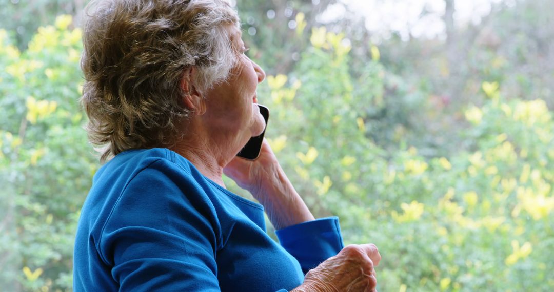 Senior Woman Talking on Phone by Window with Greenery View - Free Images, Stock Photos and Pictures on Pikwizard.com