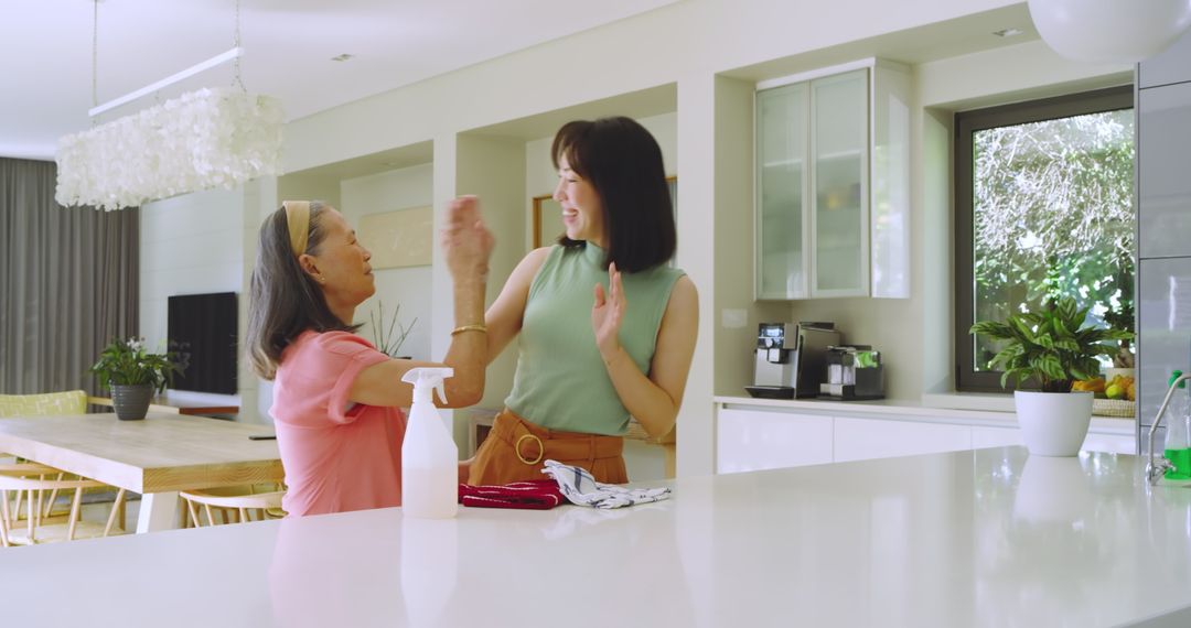 Mother and Daughter High-Fiving While Cleaning Kitchen