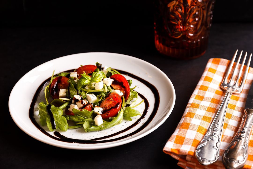 Arugula Caprese Salad with Fresh Mozzarella and Balsamic Glaze on White Plate