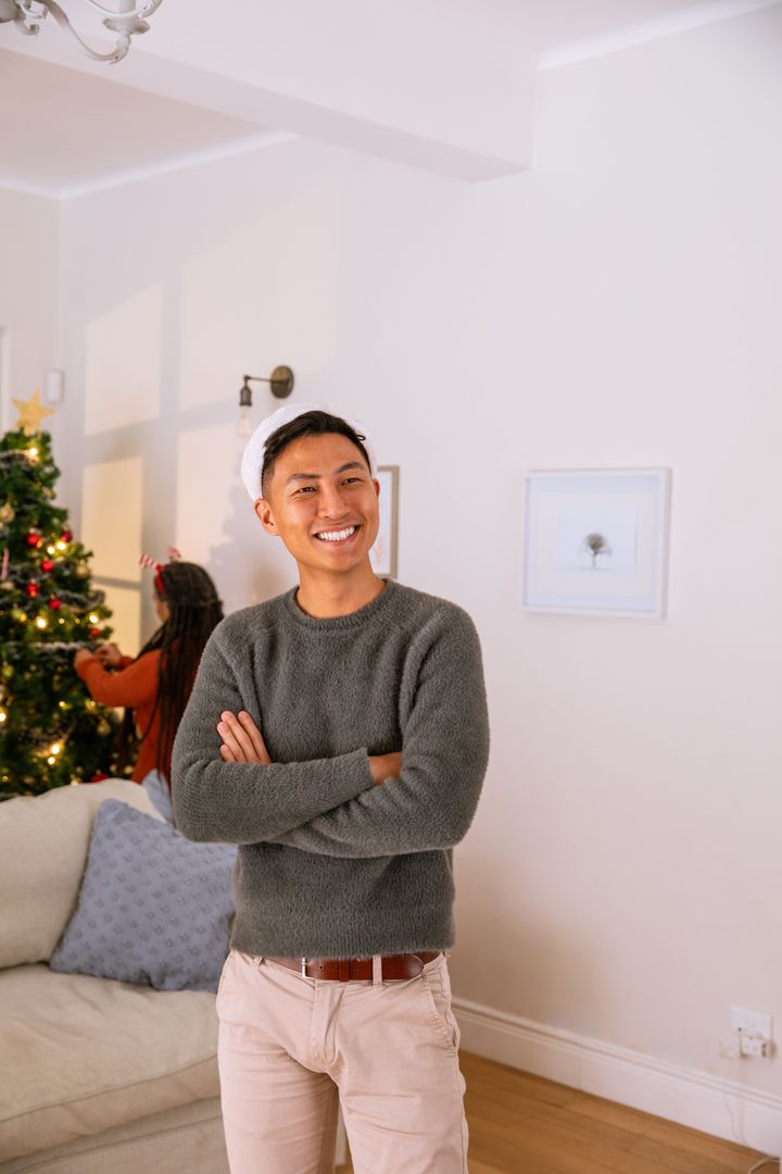 Smiling Man with Santa Hat and Friends Decorating Christmas Tree