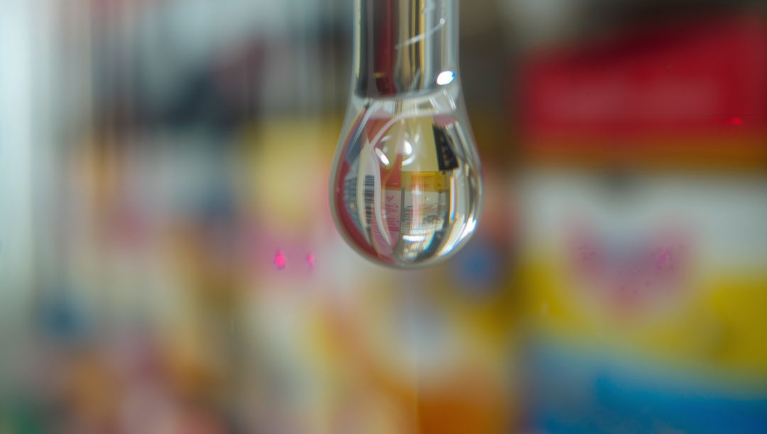 Macro droplet on pipette magnifying inverted barcode with colorful retail shelf bokeh