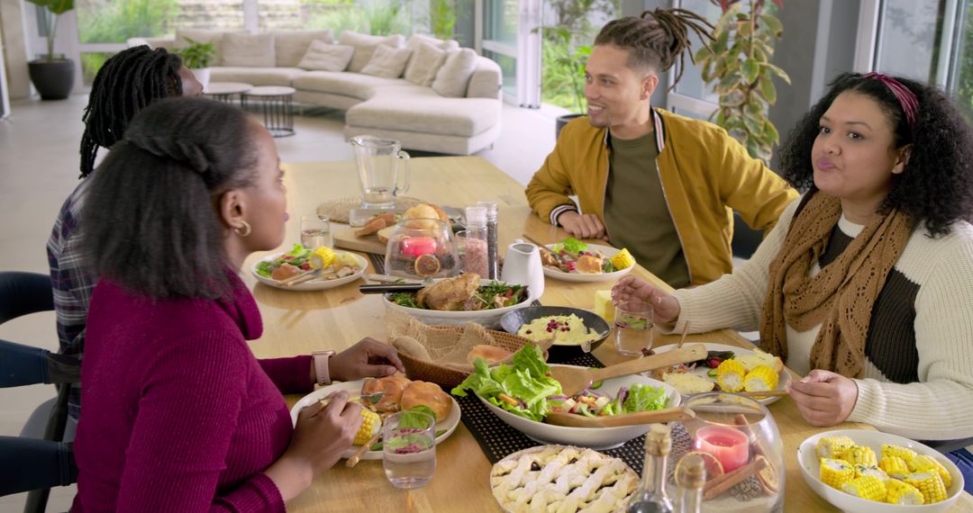 Diverse friends sharing meal around wooden dining table in sunlit modern home