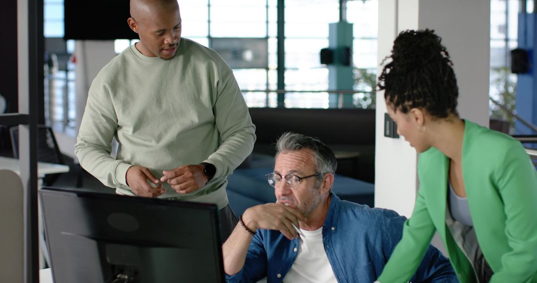 Diverse team collaborating around monitor in modern open-plan office, brainstorming ideas