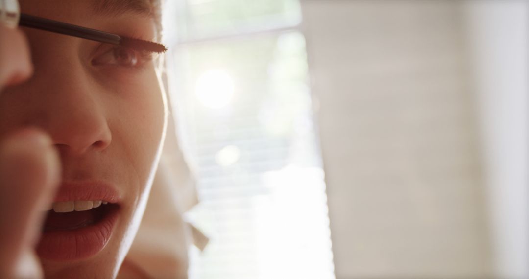 Young Woman Applying Mascara with Sunlight Streaming Through Window - Free Images, Stock Photos and Pictures on Pikwizard.com