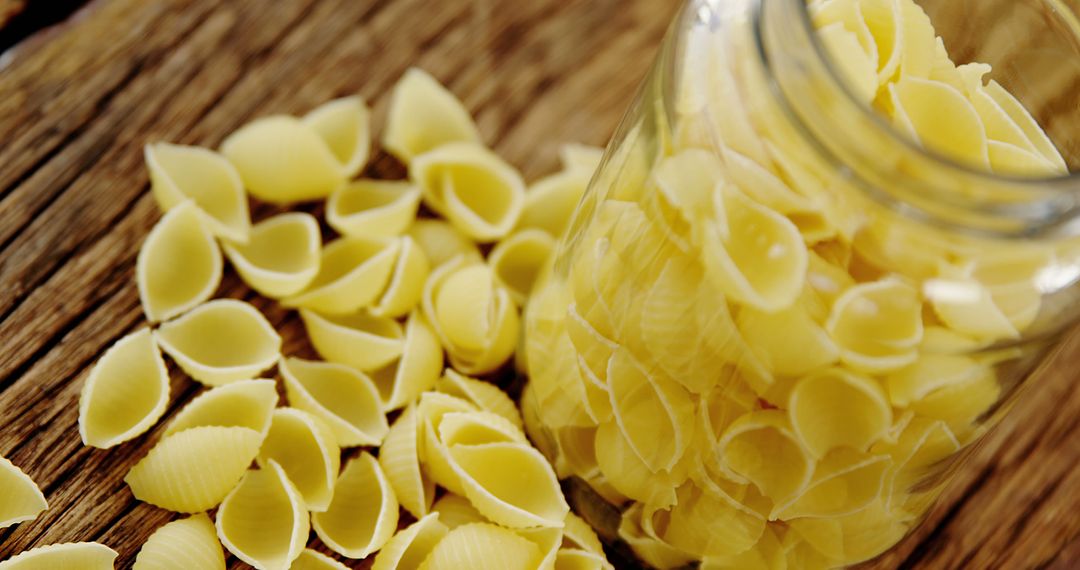 Dry Conchiglie Pasta Scattered from Glass Jar on Wooden Surface - Free Images, Stock Photos and Pictures on Pikwizard.com