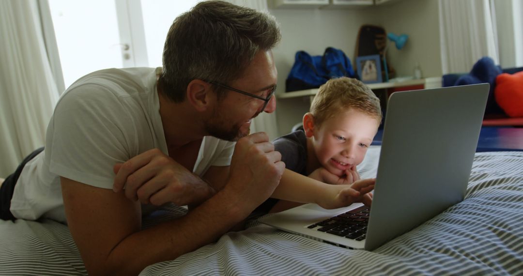 Father and Son Watching Video on Laptop While Lying on Bed - Free Images, Stock Photos and Pictures on Pikwizard.com